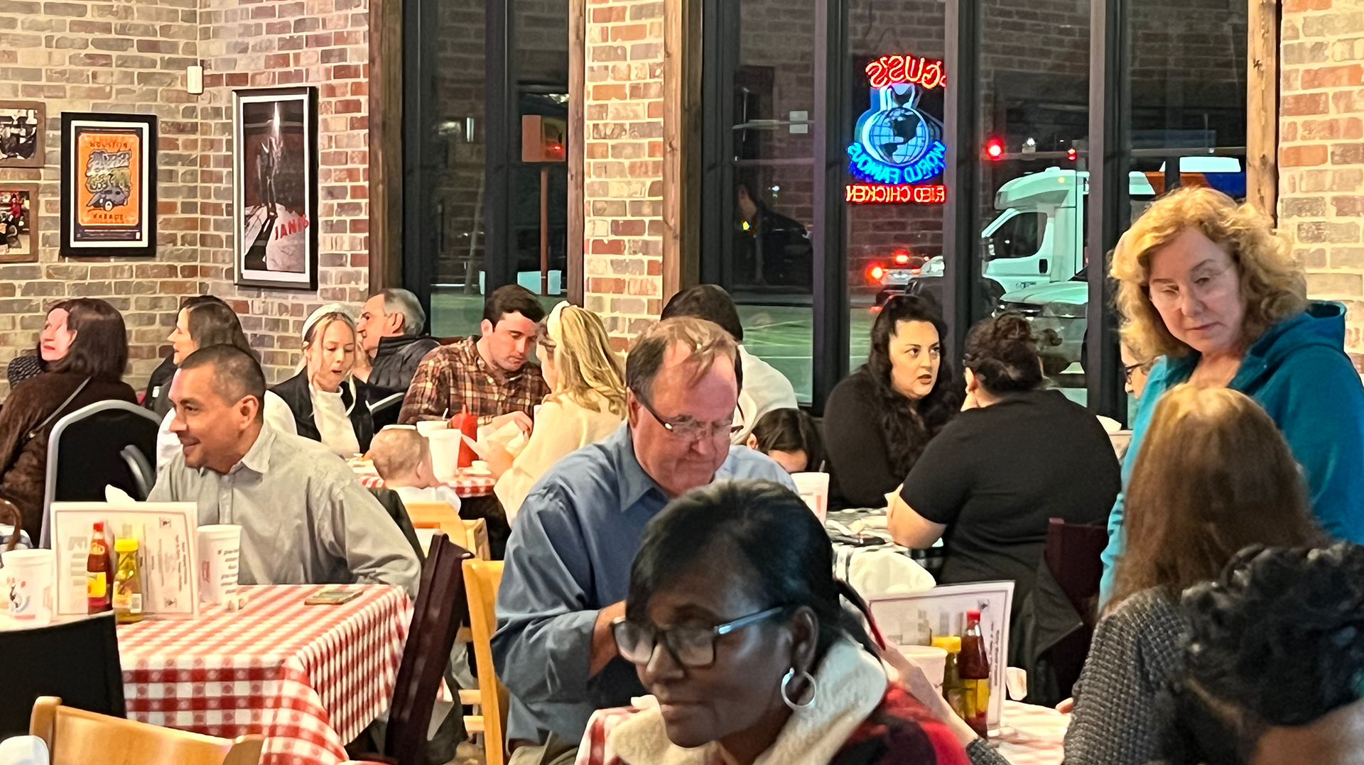 Several patrons eating inside of a restaurant with brick walls, pictures on the walls and windows showing the outside.